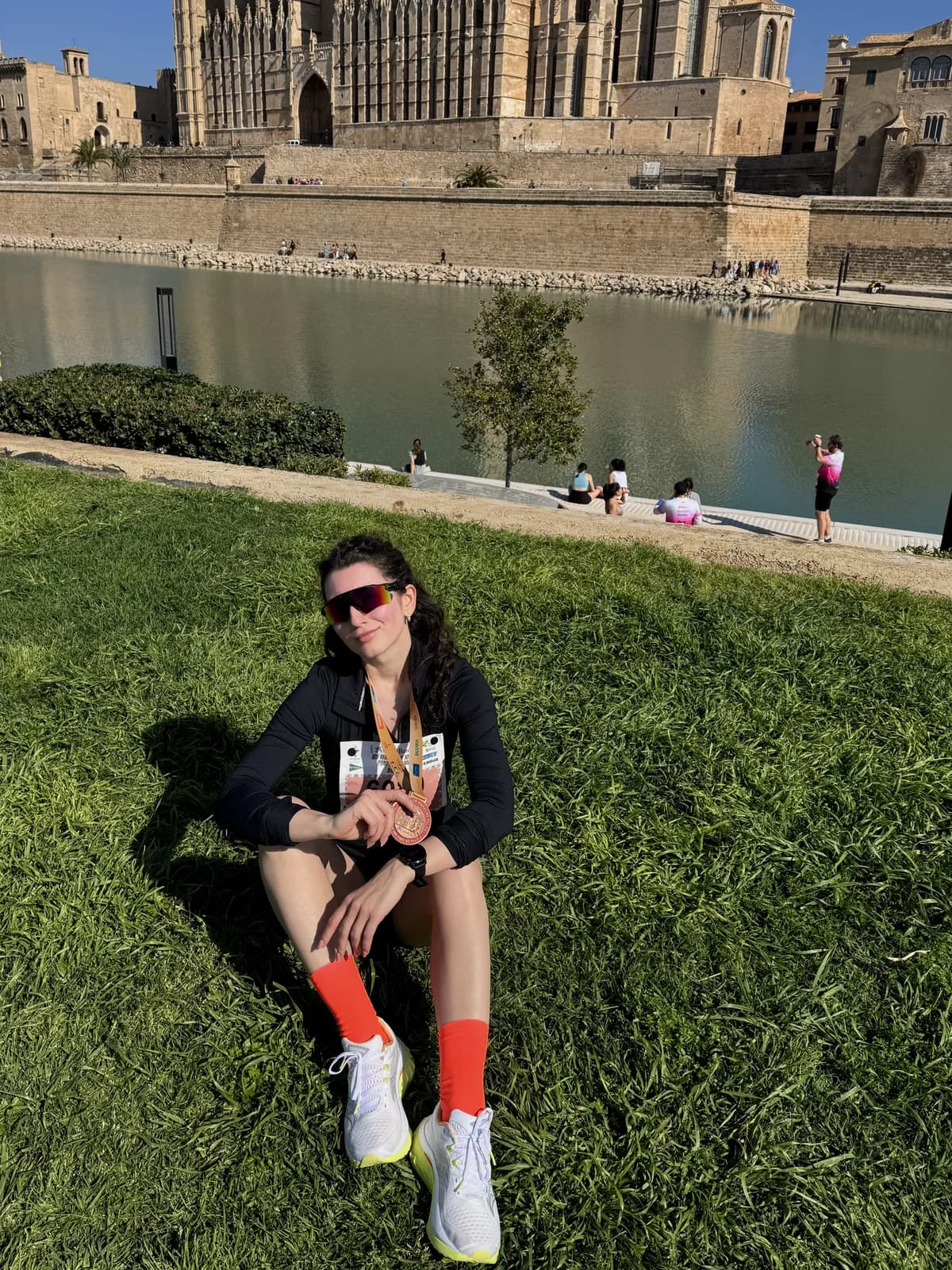 Yana in running gear resting on the grass by the cathedral in Palma de Mallorca