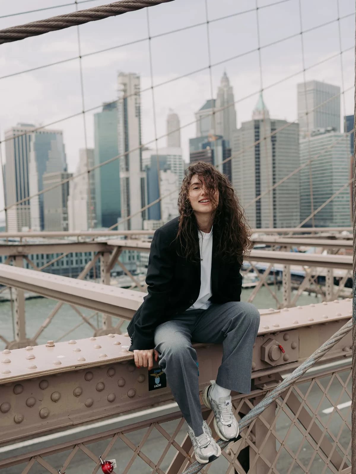 Yana sitting on the railing of the Brooklyn Bridge, the Manhattan skyline behind her